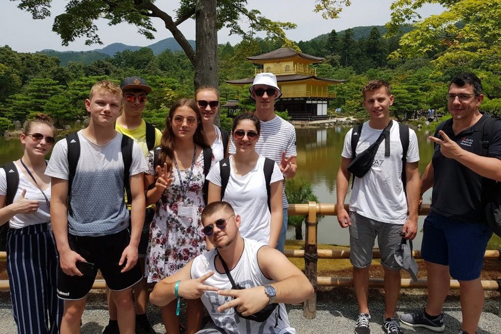 Eine Gruppe junger Personen posiert fuer ein Gruppenfoto vor einem japanischen Tempel.